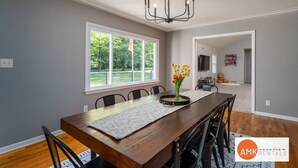 A dining room with a wooden table, chairs, a chandelier, and a window with a view of greenery. - All Decked Out Farmhouse - Game Room Nearby Beach (Holland)