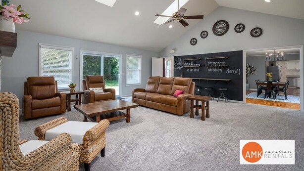 A spacious living room with a high ceiling, ceiling fan, and large windows. There is a blackboard with chalk writing on the wall and a dining area with a table and chairs. - All Decked Out Farmhouse - Game Room Nearby Beach (Holland)