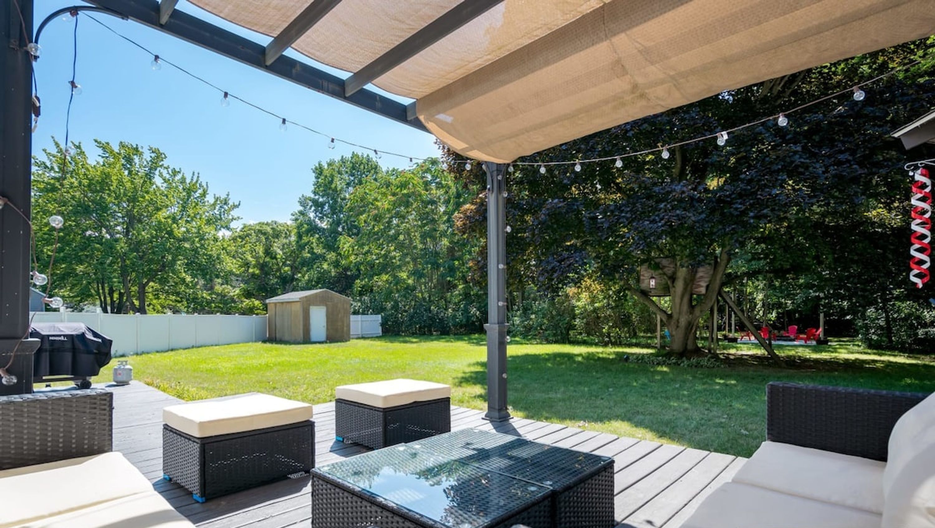 An outdoor patio area with wicker furniture, a barbecue grill, and string lights.