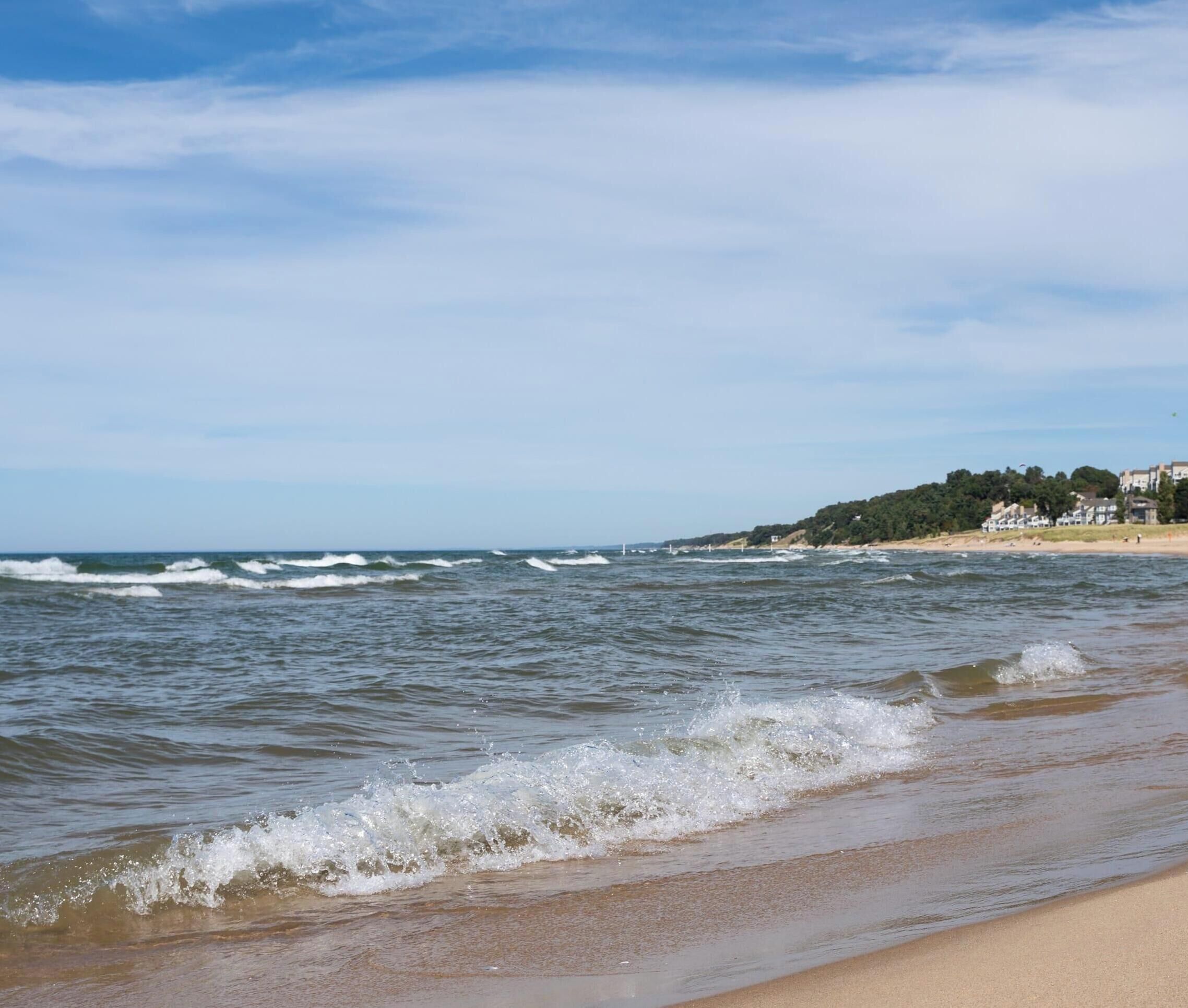 Une plage avec des vagues, une étendue de sable et des bâtiments en arrière-plan.