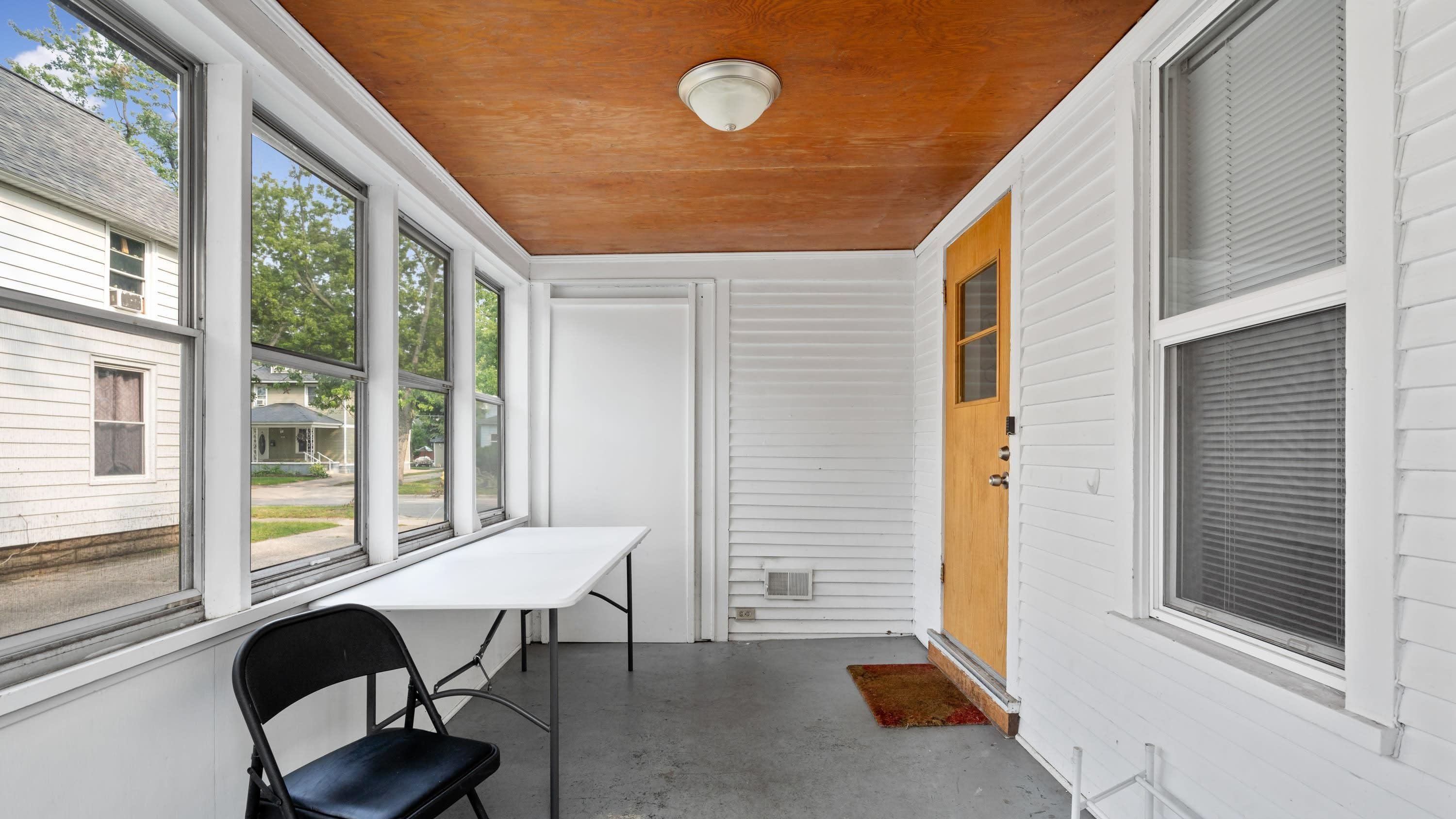 A room with a white exterior, a wooden ceiling, a white door, and a window with blinds.