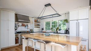 A modern kitchen with a large island, bar stools, white cabinetry, and a hanging light fixture. - Beautiful Custom Lake House (Holland)