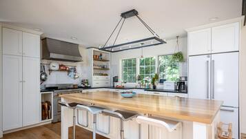 A modern kitchen with a large island, bar stools, white cabinetry, and a hanging light fixture.