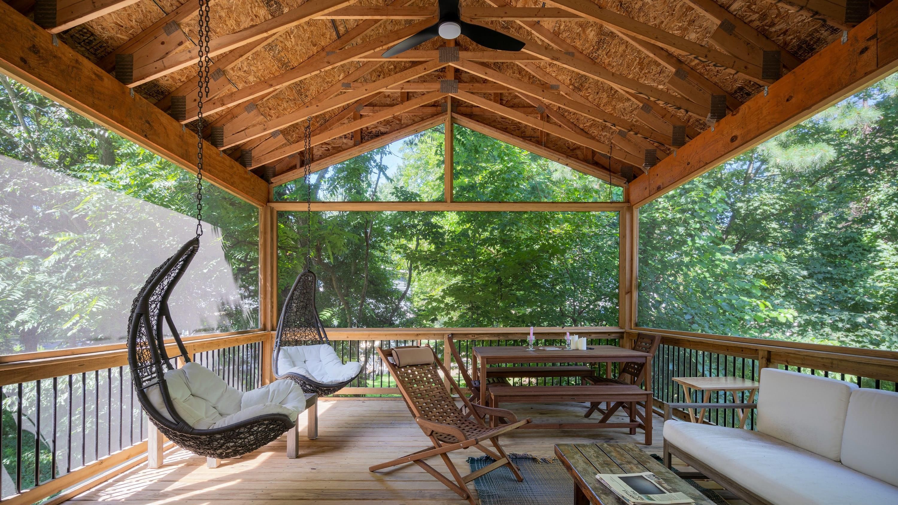 A wooden deck with a hanging chair, a cushioned chair, and a sofa.