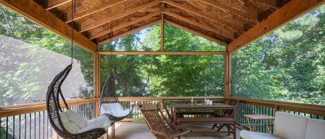 A wooden deck with a hanging chair, a cushioned chair, and a sofa.