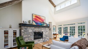 A spacious living room with a stone fireplace, a green armchair, a white sofa, and a large window with a view of the outdoors. - Beautiful Custom Lake House (Holland)