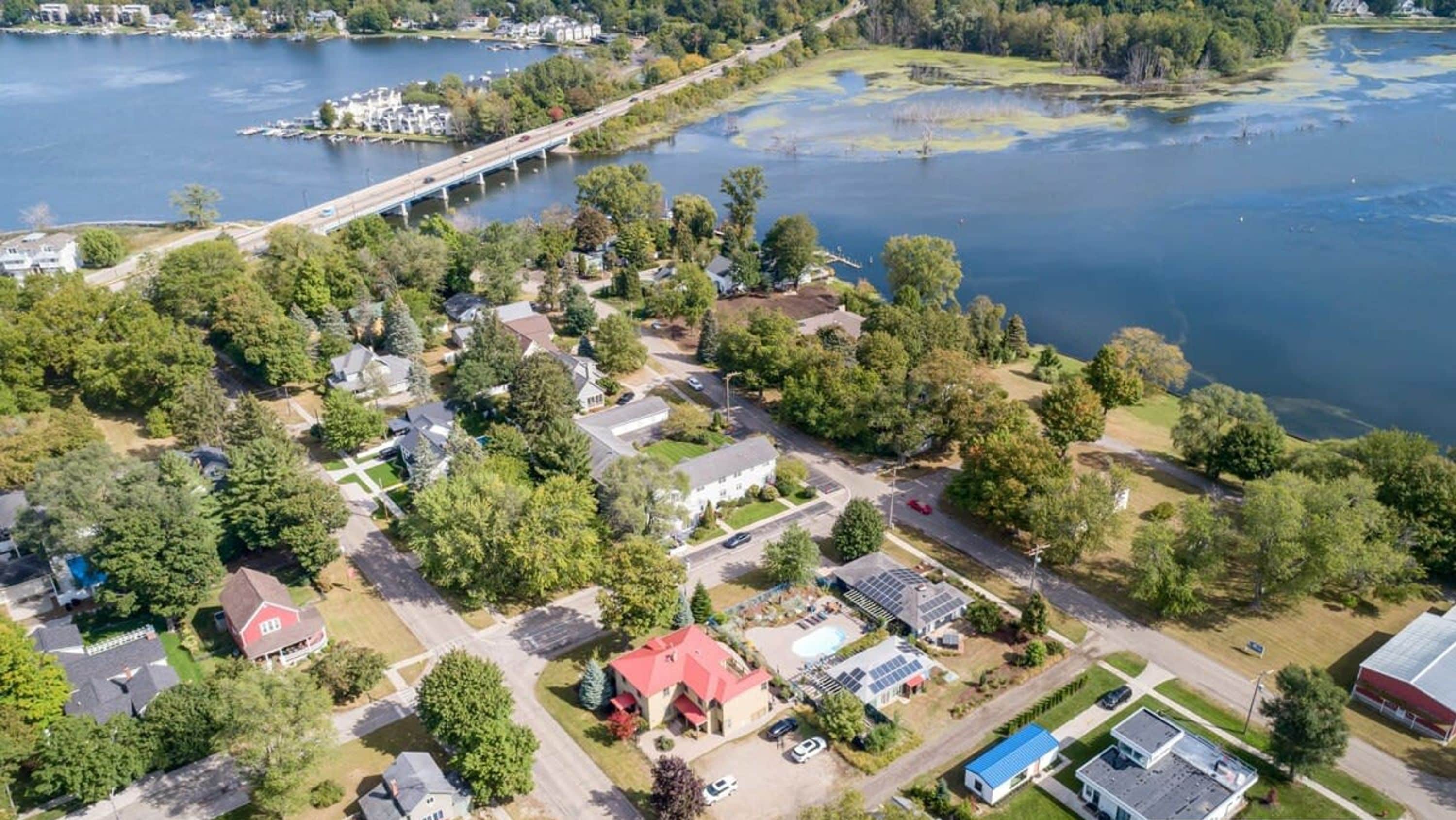 An aerial view of a residential area with houses, a dock, and a bridge over a lake.