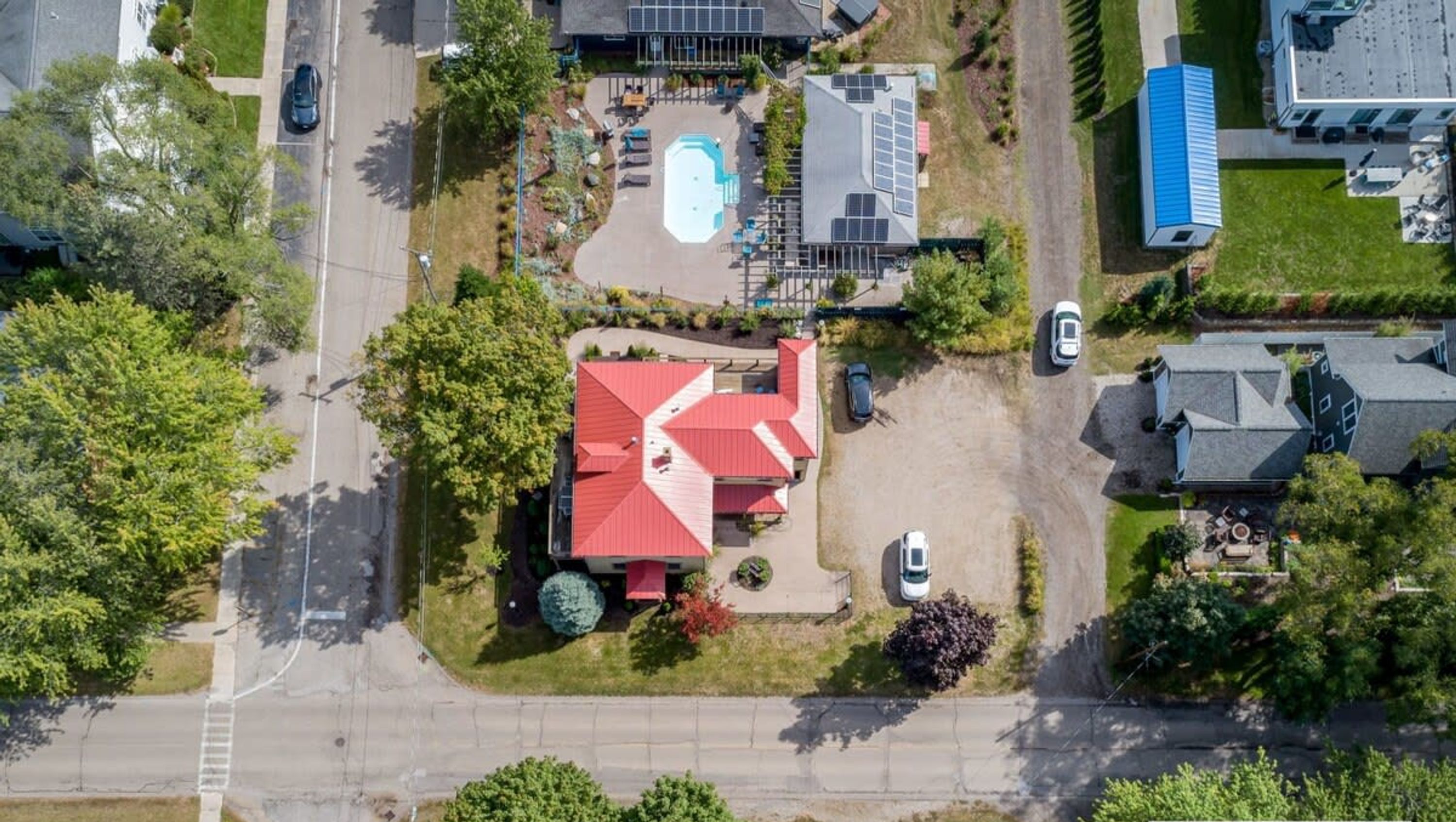 An aerial view of a residential area with a house featuring a red roof, a swimming pool, and solar panels.