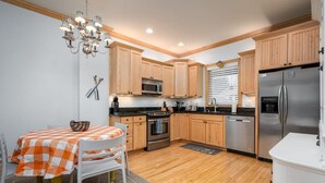 A modern kitchen with wooden cabinets, stainless steel appliances, and a dining area with a checkered tablecloth. - Lake Life Getaway - Condo Near Downtown (Douglas)