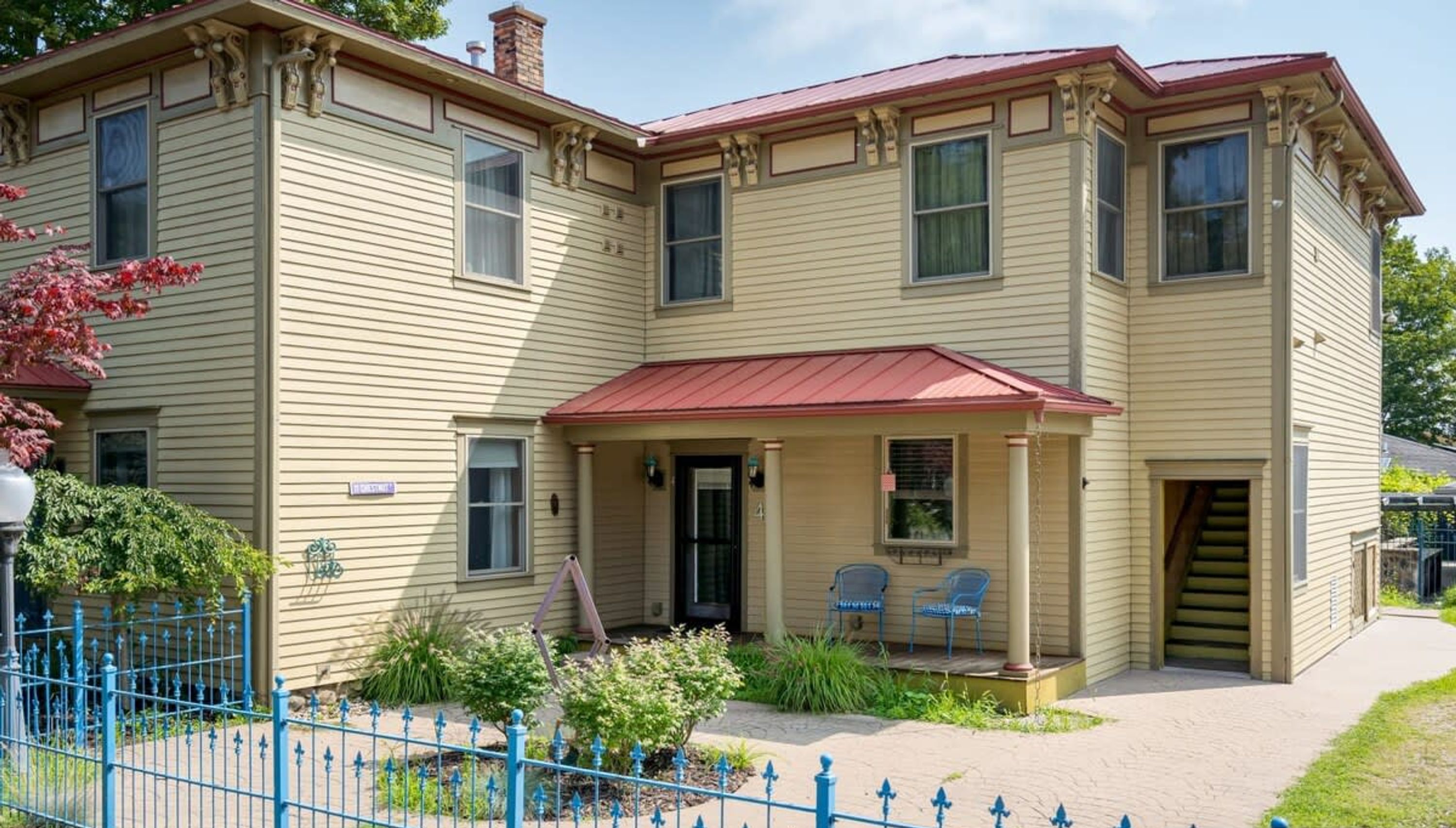 A two-story building with a beige exterior, a red roof, and a front porch with two chairs.