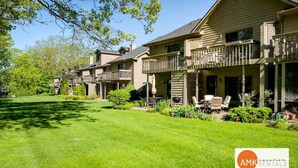 A row of two-story houses with balconies, a well-maintained lawn, and outdoor furniture. - Charming Bayview - Downtown Condo With Pool (Saugatuck)