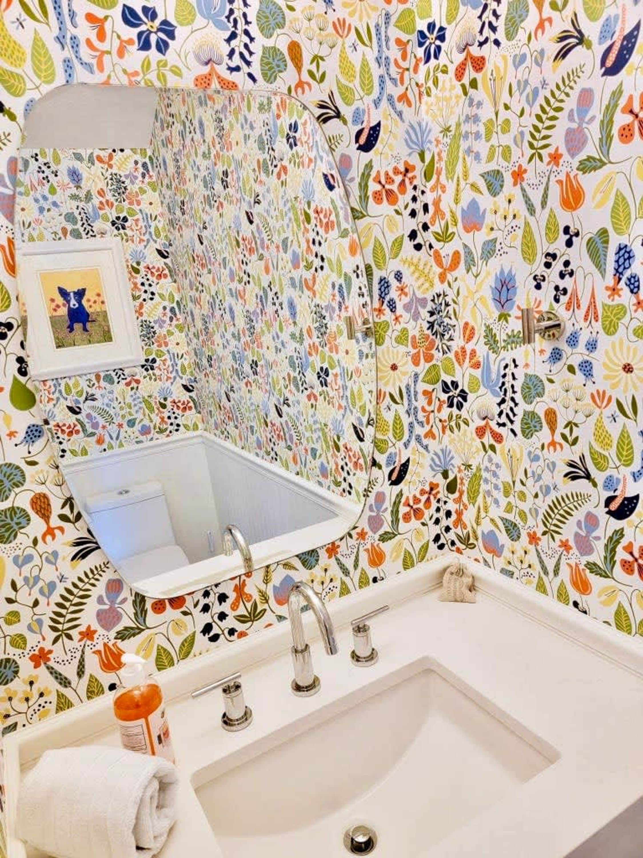 Ein Badezimmer mit einem weißen Waschbecken, einem Spiegel darüber und farbenfrohem Blumenpapier.