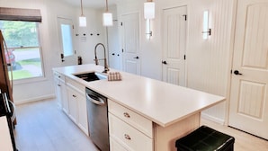A modern kitchen with white cabinetry, a central island, pendant lighting, and a view of the outdoors. - Charming Bayview - Downtown Condo With Pool (Saugatuck)
