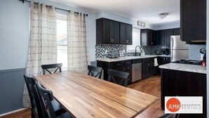 A modern kitchen with dark cabinets, a wooden dining table, and a tiled backsplash. - Holland Hideaway in Holland (Holland)