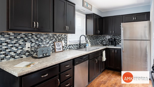 A modern kitchen with dark cabinets, a stainless steel refrigerator, and a tiled backsplash. - Holland Hideaway in Holland (Holland)