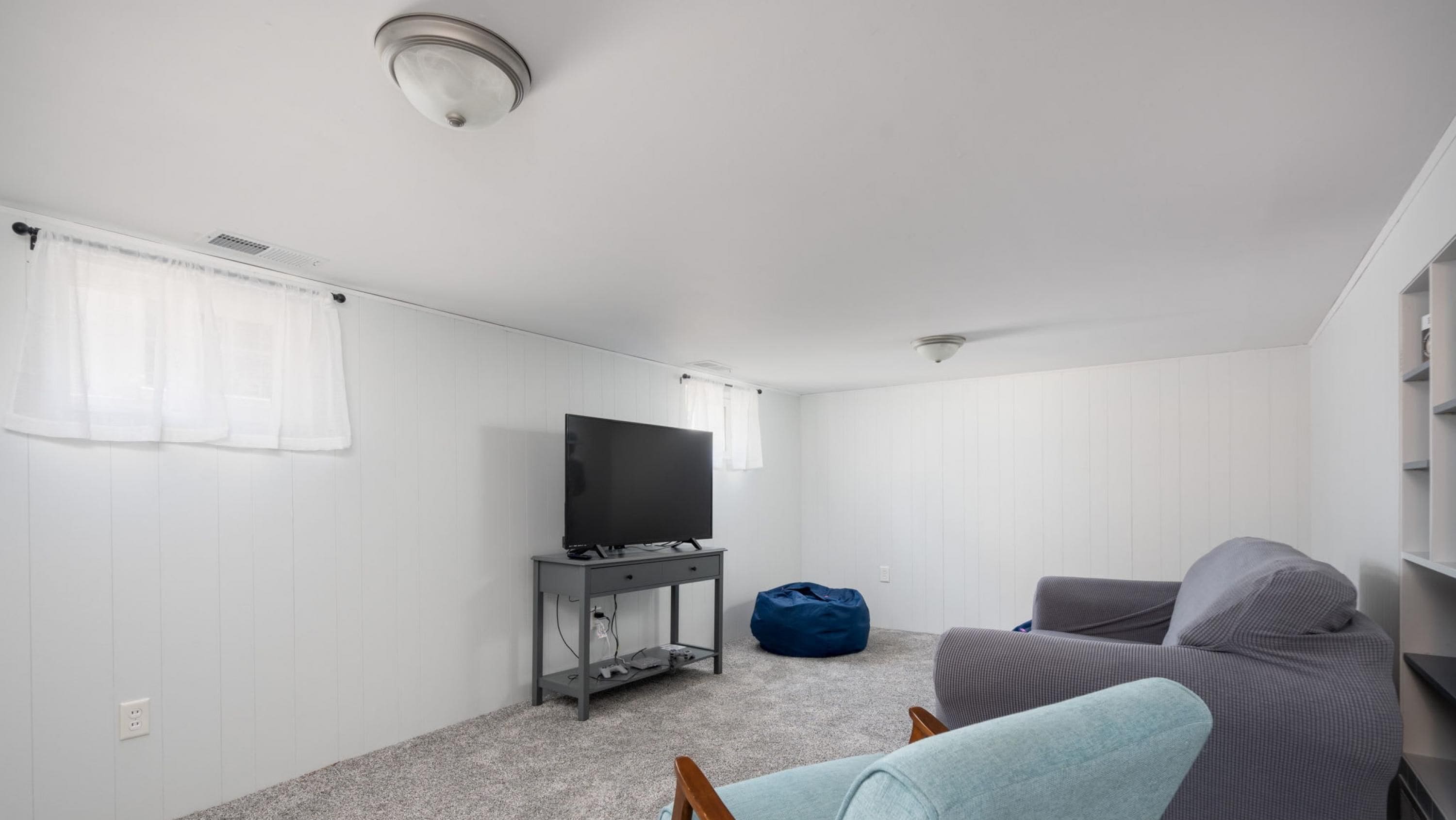 A small, modern room with a television on a stand, a bean bag, and a grey sofa.