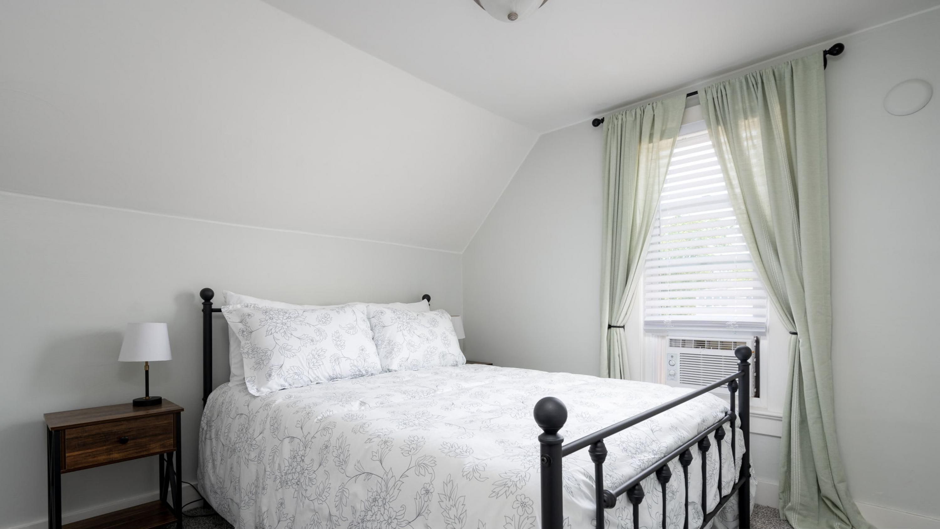A bedroom with a bed, a nightstand, a lamp, and a window with curtains.