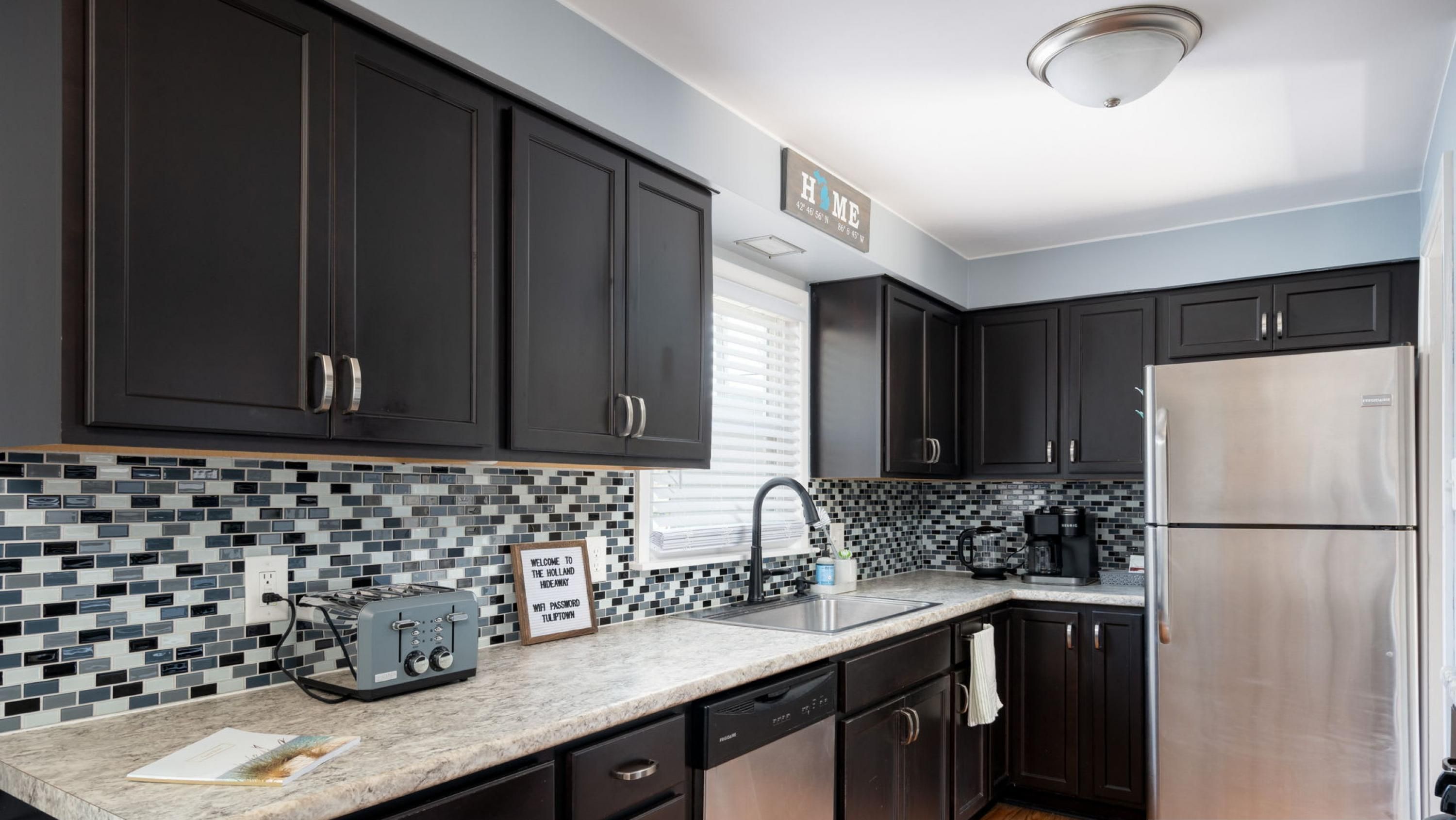A modern kitchen with dark cabinets, a stainless steel refrigerator, and a tiled backsplash.