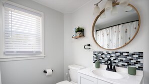 Ein Badezimmer mit Toilette, Waschbecken, Spiegel und Fenster mit Jalousien.