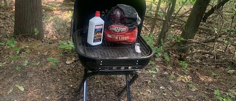 Una parrilla portátil con carbón y un saco de carbón Kingsford en una zona boscosa.