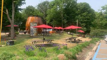 A park with picnic tables, red umbrellas, and a large barrel labeled 'Douglas Root Beer Barrel'.
