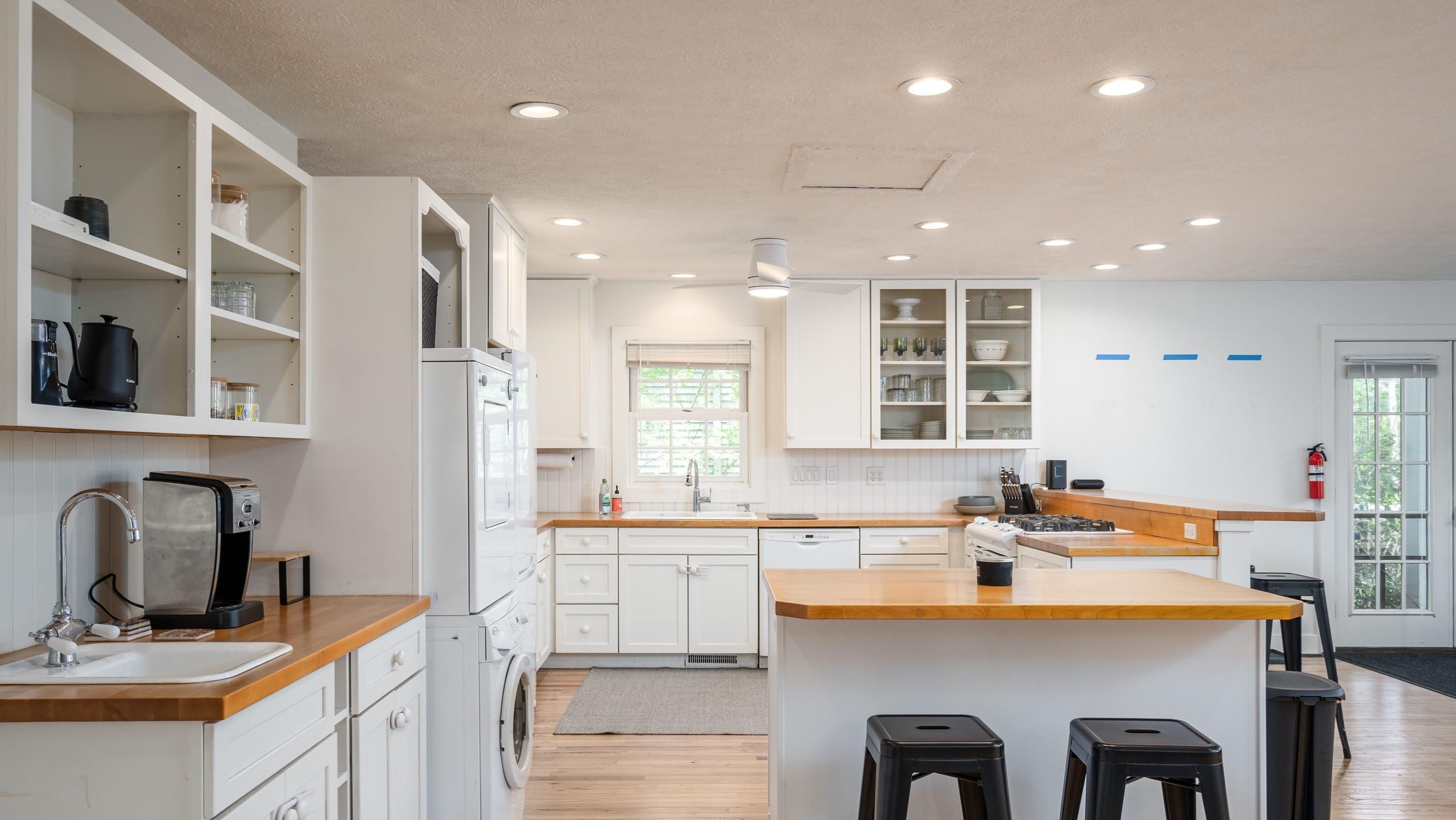 Una cocina moderna con armarios blancos, encimeras de madera y una isla central con taburetes.