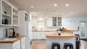 A modern kitchen with white cabinetry, wooden countertops, and a central island with stools. - Tate House in Saugatuck (Saugatuck)