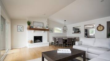 A modern living room with a fireplace, a dining area, and a kitchen in the background.