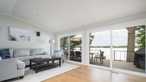 A modern living room with a sofa, coffee table, and a view of a deck and lake. - The Glistening Grape - Lakeside Getaway (Fennville)