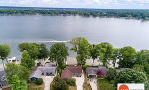 A residential area with houses near a lake, a boat on the water, and a logo in the bottom right corner. - The Glistening Grape - Lakeside Getaway (Fennville)