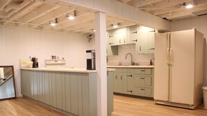 A modern kitchen with light wood flooring, a central island, and a large refrigerator. - Miner Lake Lakefront Beach Cottage for Family Fun (Allegan)