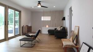 A modern living room with a ceiling fan, a sofa, a coffee table, and a bench. - Miner Lake Lakefront Beach Cottage for Family Fun (Allegan)