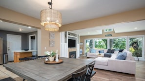 A modern living room with a wooden dining table, a sofa, and a large window offering a view of the outdoors. - Lakeside Retreat - Waterfront Quiet Neighborhood (Muskegon)