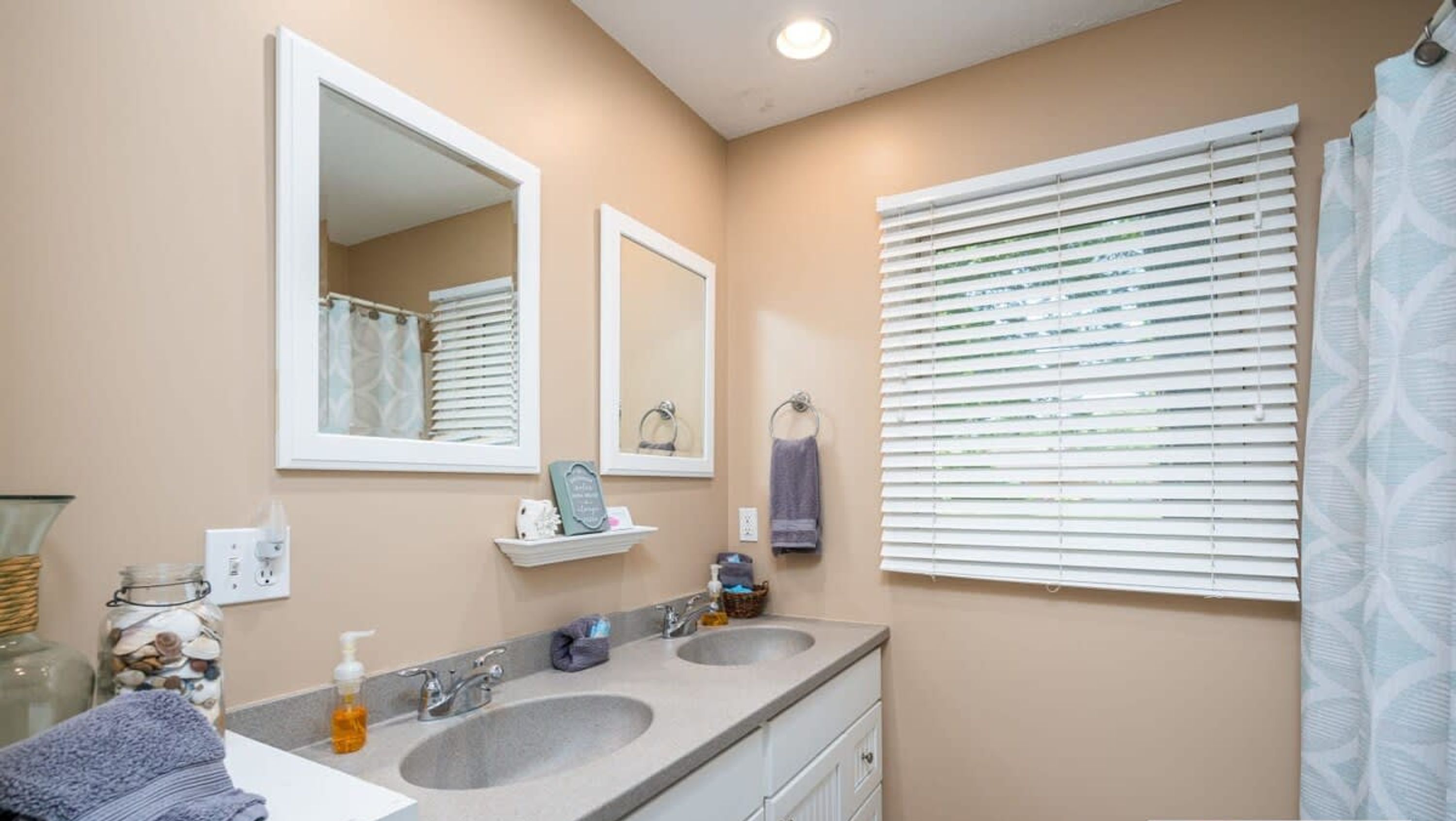 A bathroom with two sinks, a mirror, a towel rack, and a window with blinds.