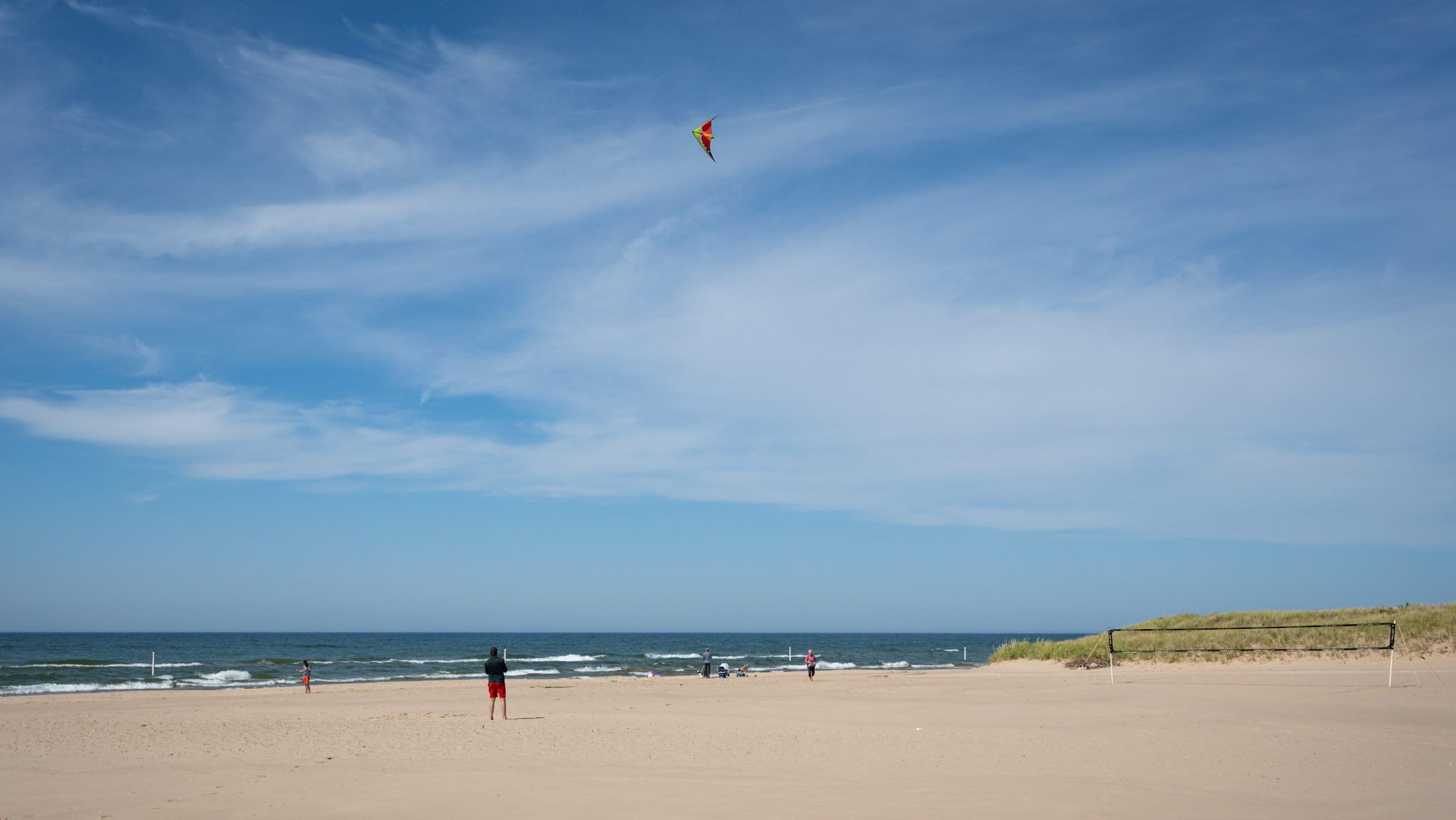 A beach with a clear sky, a kite flying, and a logo for AMK Rentals.