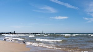 A beach with waves, a lighthouse, and a pier.
