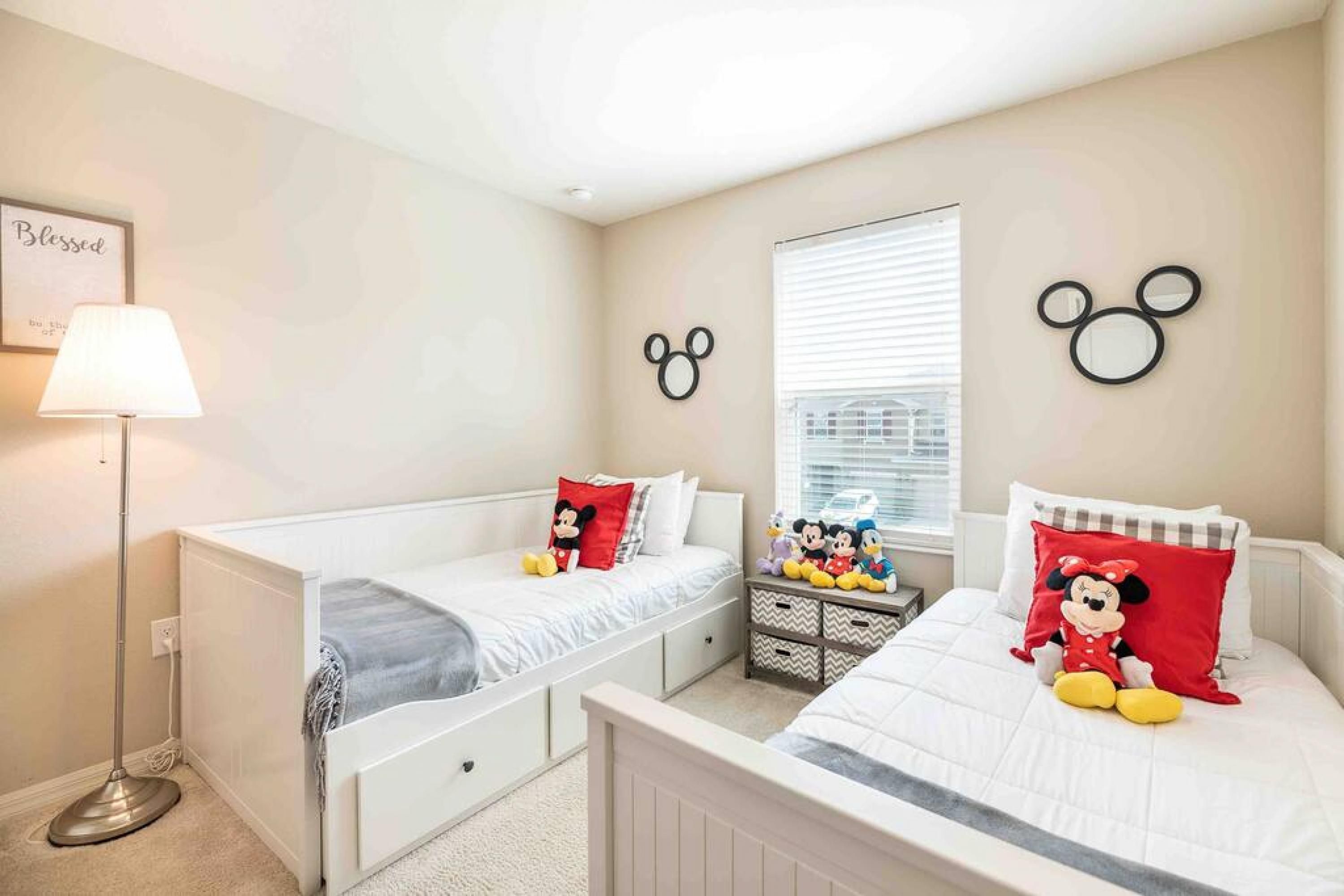 A bedroom with two beds, a nightstand with Mickey Mouse figurines, and a wall with Mickey Mouse head silhouettes.