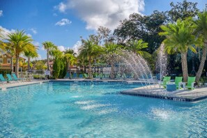 A swimming pool with a water feature, surrounded by palm trees and lounge chairs.