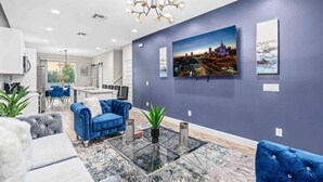 Un salon moderne avec un canapé bleu, une table basse en verre et un tableau représentant un paysage urbain accroché au mur.