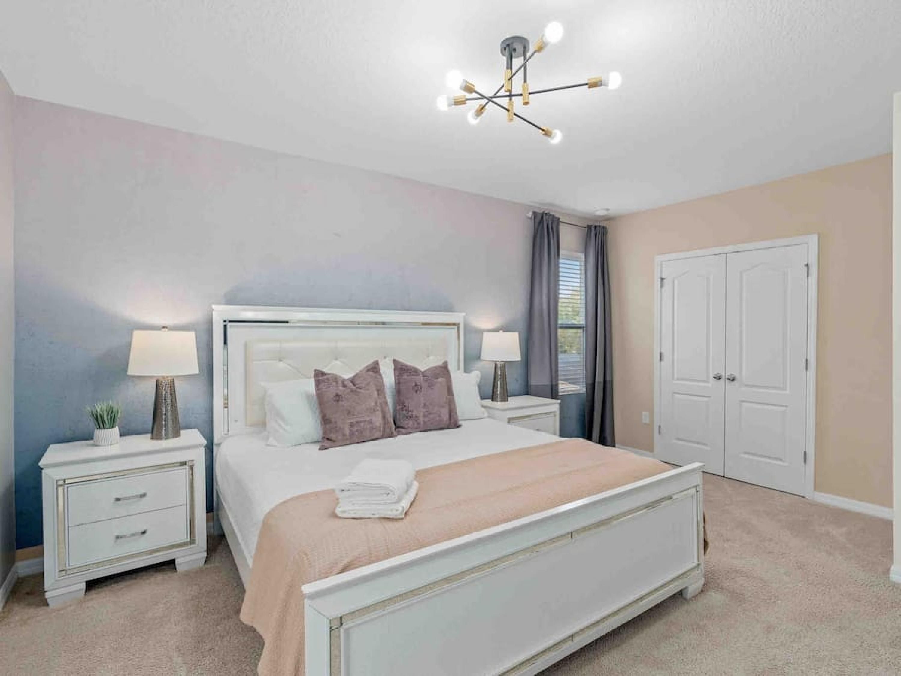 A bedroom with a bed, nightstands, a lamp, a ceiling light fixture, and a door.