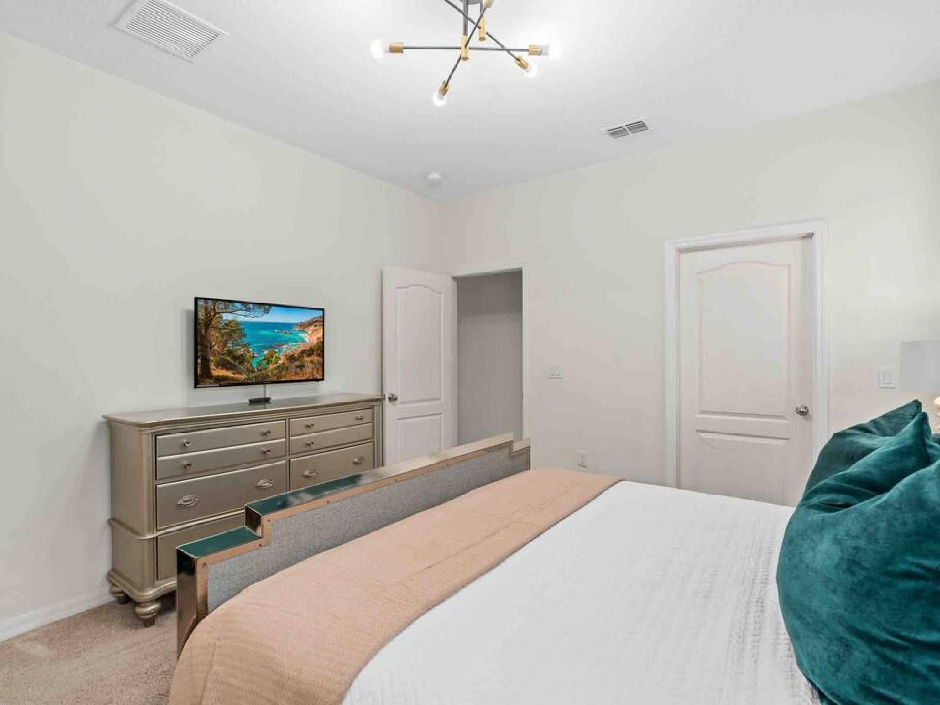 A bedroom with a bed, a dresser, a television on the wall, and two doors.