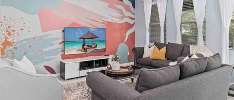 A living room with a grey sofa, a white armchair, and a coffee table. There is a painting of a beach scene on the wall.