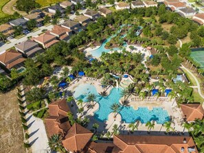 An aerial view of a resort with multiple swimming pools, palm trees, and residential buildings.