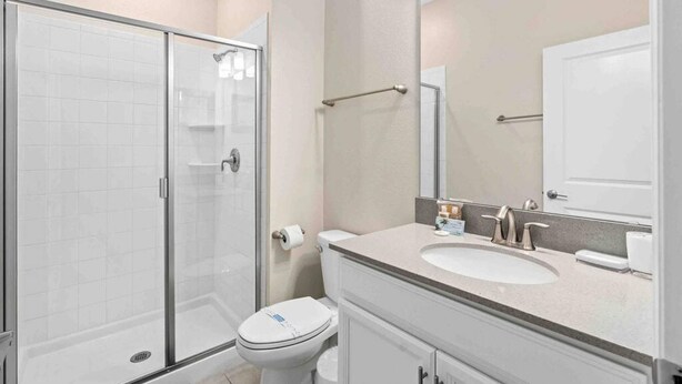 Un baño con cabina de ducha de vidrio, inodoro, lavabo con espejo y un perchero para toallas.