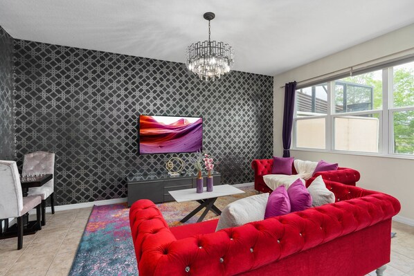 A modern living room with a red sofa, a TV mounted on the wall, and a patterned wallpaper. - Super Fun-colors Gameroom Lakeviews Sleeps 13 (Kissimmee)
