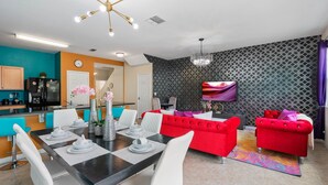 Una sala de estar moderna con un sofá rojo, sillas blancas, una mesa de comedor con platos y un televisor montado en la pared.
