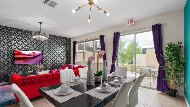 Habitación de hotel moderna con comedor, un sofá rojo, televisión y balcón con cortinas moradas.