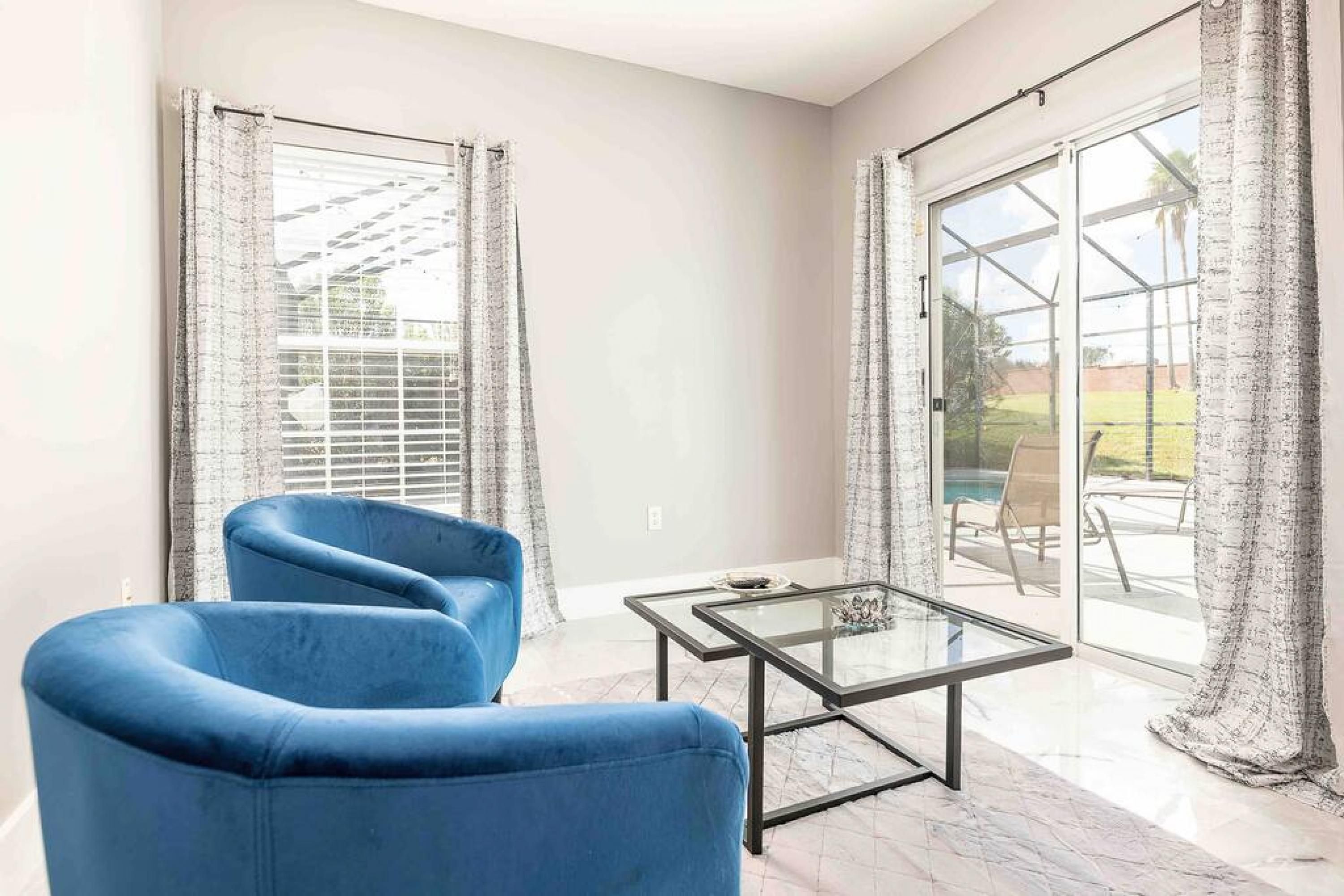 A modern living room with a blue sofa, a glass coffee table, and large sliding glass doors leading to a patio area.