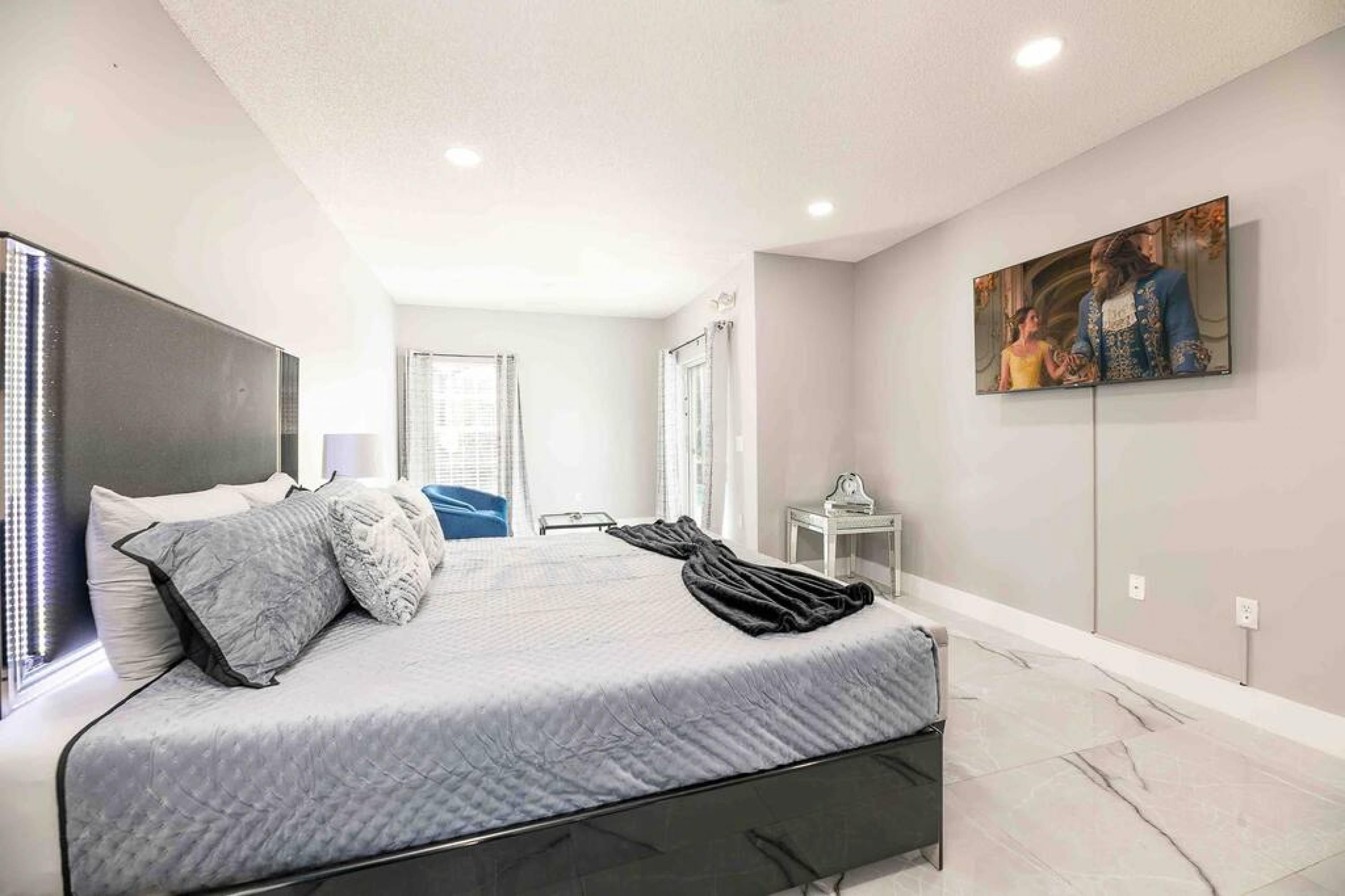 A modern bedroom with a large bed, a flat-screen TV, and a painting on the wall.