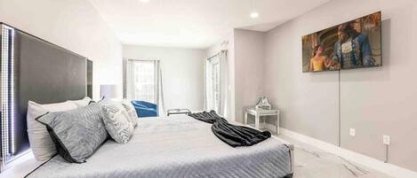 A modern bedroom with a large bed, a flat-screen TV, and a painting on the wall.
